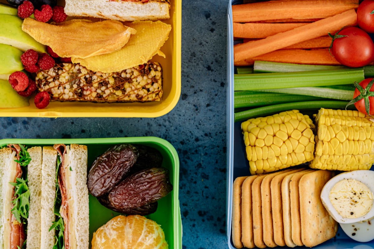 A person packing a colorful vegetable wrap into a compact lunchbox