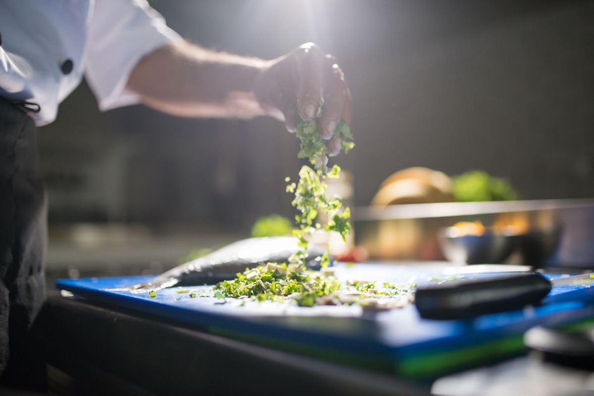 A sharp stainless steel chef knife slicing fresh vegetables on a wooden cutting board.